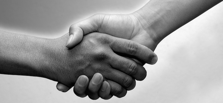 A black and white photo of two people shaking hands in a welcoming gesture.